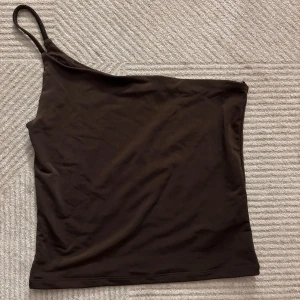 Brun oneshoulder topp från BikBok - Snygg brun oneshoulder topp från BikBok. Passar i alla tillfällen.                                              Köpt för någon månad sedan men inte använt någon gång tyvärr❣️