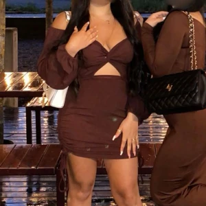 Brun klänning med knytning - Snygg brun klänning med långärmade ärmar och knytning framtill. Den har en tight passform och kort längd, perfekt för en kväll ute. Klänningen har en stilren design med en liten öppning vid bysten.🤗använd en gång 