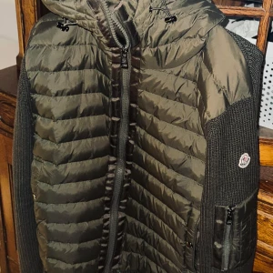 Moncler hooded cardigan  - Snygg grön jacka från Moncler med quiltad design och stickade ärmar. Jackan har en dragkedja framtill och en praktisk ficka med dragkedja på ärmen. Perfekt för kyligare dagar med sin stilrena look och varma material. Storlek XL men sitter som en L.