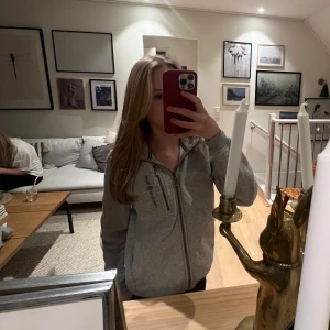 Grå hoodie från sail raicing - Säljer en grå hoodie från sail racing med dragkedja och logga på bröstet. Tröjan har långa ärmar och en bekväm passform. Perfekt för en avslappnad stil.