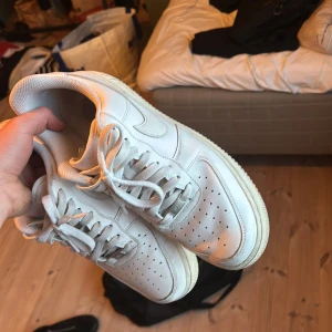 Vita Nike Air Force sneakers - Säljer ett par klassiska vita Nike Air Force sneakers. Skorna har en stilren design med snörning och perforerade detaljer på tån för extra ventilation. Perfekta för en avslappnad och trendig look.