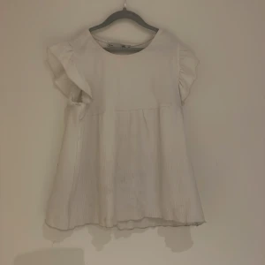 Vit blus med volangärmar från 157 - Säljer en söt vit blus från 157 med volangärmar. Blusen har en luftig passform och är perfekt för varmare dagar. Den är tillverkad i ett lätt och bekvämt material som ger en avslappnad look.