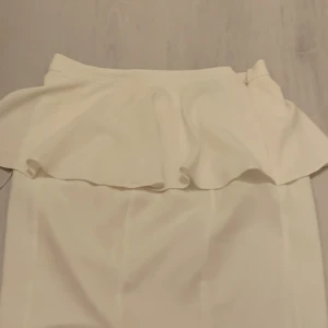 Vit kjol från Topshop - Säljer en stilren vit kjol från Topshop i storlek EUR 38. Kjolen har en volangdetalj upptill och en diskret dragkedja baktill för enkel påklädning. Perfekt för en chic look!