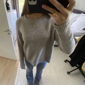 Grå stickad tröja - Mysig grå stickad tröja med rund hals och långa ärmar. Perfekt för kyligare dagar och enkel att matcha med olika outfits. Tröjan har en avslappnad passform och ribbade kanter vid ärmslut och nederkant.