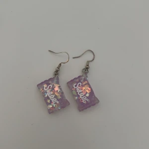 Lila örhängen med glitterdetaljer - Unika lila örhängen med glittrande detaljer och texten 'Sweet' på framsidan. De har en rektangulär form och hängs på krokar. Perfekta för att ge en färgglad touch till din stil.
