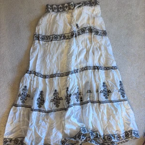 Vit långkjol från Zara - Säljer en vacker vit långkjol från Zara med svart broderat mönster. Kjolen har en elastisk midja med knytband och dekorativa broderier längs med kjolen. Perfekt för en bohemisk look! Inte struken just nu så ni tänker på de. Säljer pågrund av flytt och för mycket kläder 😁
