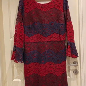 Röd och blå spetsklänning från Yumi - Säljer en elegant röd och blå spetsklänning från Yumi. Klänningen har långa ärmar med volangdetaljer. Perfekt för speciella tillfällen med sin unika färgkombination och stil.