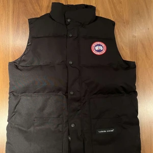 Svart dunväst från Canada Goose - Säljer en svart dunväst från Canada Goose med knappar och dragkedja. A kopi. Säljer för den då inte passar mig. Super bra kvalité storlek M.