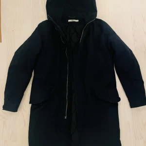 Svart parkajacka från Hope - Säljer en stilren marinblå parkajacka från Hope. Jackan har en quiltad insida och dragkedja framtill. Den är långärmad och har en praktisk huva. Perfekt för kyligare dagar.