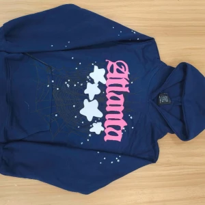 Mörkblå hoodie med tryck - Säljer en mörkblå hoodie från SP5R med ett coolt tryck av vita stjärnor och rosa text på framsidan. Perfekt för en avslappnad stil. Hoodien har en klassisk passform med långa ärmar och en bekväm huva.