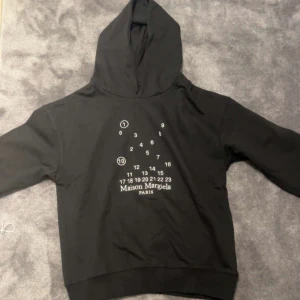 Svart hoodie från Maison Margiela - Snygg svart hoodie från Maison Margiela med deras ikoniska nummertryck på framsidan. Tillverkad i Italien, perfekt för en riktigt skön outfit . Skönt material och riktigt varm! Har av er vid frågor eller funderingar!