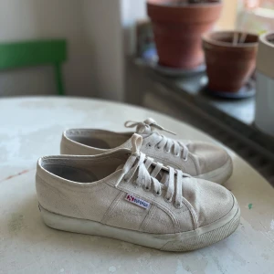 Beigea skor från Superga - Säljer ett par stilrena tygskor från Superga i storlek 40, knappt använda. Skorna är i en klassisk design men med en snygg lite högre sula. Perfekta i vår och sommar. 