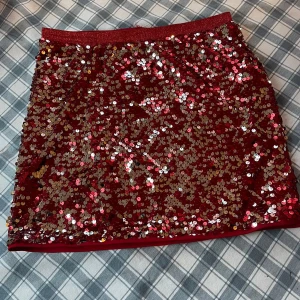 Röd paljettkjol  - Snygg röd kortkjol täckt med glittrande paljetter. Perfekt för att sticka ut på festen. Elastisk midja för bekväm passform. Från Lindex, storlek 170 kids men passar att ha om man inte är barn också.  Finns ett litet hål visar med bild, syns inte när man ha på. Går att fixa lätt också! 