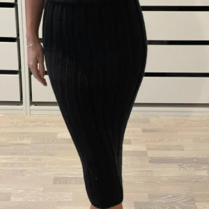 Svart ribbad kjol - Snygg svart ribbad kjol i tight passform. Kjolen är stickad och har en elegant längd som passar perfekt för olika tillfällen. Den är både stilren och bekväm, vilket gör den till ett mångsidigt plagg i garderoben.