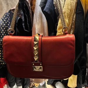 Glam Lock Valentino Garvani väska röd - Säljer min otroliga Glam Lock Valentino Garvani väska Både dustbag och kvitto tillkommer.  Köpte den second hand för närmare 10 000, säljer för 8000kr pga de lilla hålet i botten. Det går att laga lätt och inte särskilt dyrt hos en väskmakare!  Buda gärna är flexibel  Den är röd och vit på insidan  Nitar på  Går att han crossbody eller på axeln En av mina absolut favorit väskor men använder inte den inte lika mycket längre.