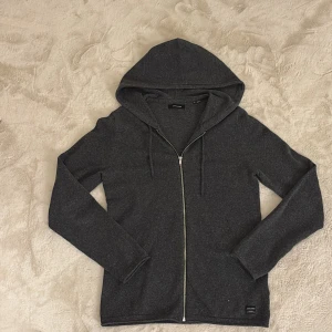 Grå hoodie från Jack & Jones - Säljer en stilren grå stickad hoodie från Jack & Jones med dragkedja framtill. Perfekt för en avslappnad look. Den har en praktisk huva och långa ärmar. Väldigt populär så passa på. Hör av dig vid funderingar och pris kan diskuteras vid snabb affär mvh Malte 