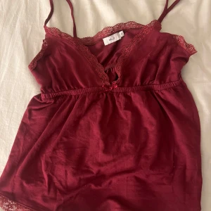 Vinröd linne från Nelly - Säljer ett vinrött linne från Nelly med spetsdetaljer längs kanterna och smala axelband. Perfekt för en elegant och bekväm look. 💖