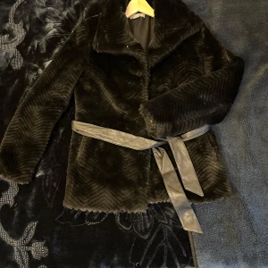 Svart pälsjacka från H&M - Säljer en elegant svart pälsjacka från H&M i storlek S. Jackan har ett snyggt mönster och ett bälte i midjan för en stilren look. Perfekt för kyliga dagar när du vill hålla dig varm och trendig. 🖤