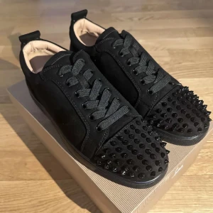 Svarta Louboutins med spikar!  - Snygga svarta sneakers med nitar på tån och röd sula. Skorna har snörning och en stilren design som sticker ut. Perfekta för att ge din outfit en edgy touch. Nypris 9 tusen! Box medföljer! Aldrig använda pga för stora!  Kvitto finns! 