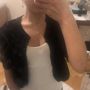 Svart bolerotopp från Zara - Säljer en sött svart bolerotopp från Zara med volangdetaljer. Perfekt för att lägga till en touch av stil till din outfit. Toppen är kortärmad och har en fin struktur som ger en unik look. Använd endast 1 gång så är i utmärkt skick . 