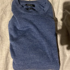 Blå merinoulltröja  - Säljer en stilren blå tröja i 100% merinoull från Galeries Lafayette. Riktigt fet och funkar till allt. Var ett litet hål på ena ärmen som är lagat, annars 10/10 skick. 