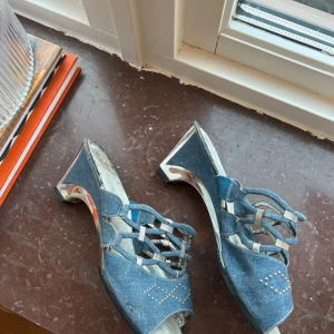 Blå kitten heels - Kitten heels i jeansmaterial med silverdetaljer och öppen tå. Köpt på vinted men för små för mig som har något breda fötter, så storleken är 40 men skulle nog passat 39 mer. Då defekter förekommer är priset så låg.