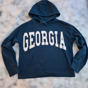 Mörkblå hoodie med texten 'GEORGIA' - Säljer en snygg mörkblå hoodie med stor vit text på framsidan. Hoodien har en klassisk design med huva och snöre. Perfekt för en avslappnad stil. ⭐️