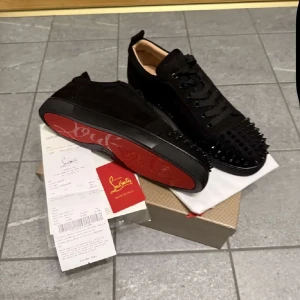 Svarta sneakers med nitar - Snygga svarta sneakers från Christian Louboutin med nitar på ovansidan. Skorna har en klassisk röd sula och är tillverkade i skinn. Perfekta för att ge en edgy touch till din stil.