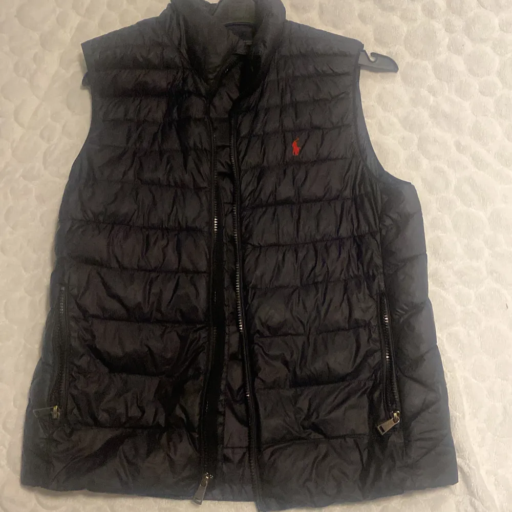 Snygg svart dunväst från Polo Ralph Lauren. Perfekt för kyligare dagar och enkel att matcha med andra plagg. Västen har knappt används och säljer den för den är för liten. Skriv privat för fler bilder. Funkar både XS/S då den är liten i storlek.. Takit.