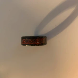 Svart ring  - Svart ring med röda detaljer. Osäker på storlek men ganska stor