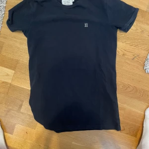 Svart t-shirt från Les Deux - Säljer en snygg svart t-shirt från Les Deux. Den är i nyskick och har en liten vit broderad detalj på bröstet. Perfekt för både vardag och fest!