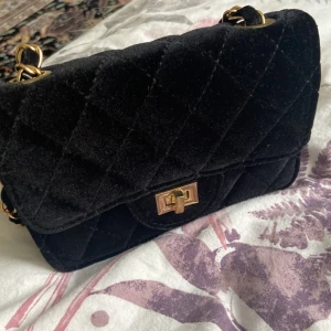 Svart quiltad axelväska med gulddetaljer - Säljer en superfin svart axelväska. Väskan har en snygg guldkedja som axelrem och ett elegant guldfärgat spänne på framsidan. Perfekt för både vardag eller fest. :)