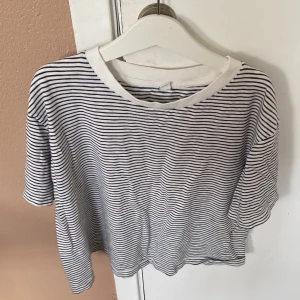 Randig t-shirt från Uniqlo - Säljer en randig t-shirt från Uniqlo i storlek S. Den är vit med svarta ränder och har korta ärmar. Perfekt för en avslappnad vardagslook! köparen betalar för frakt!