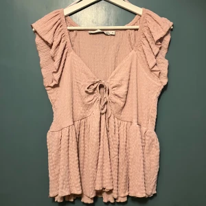 Rosa topp från 157 - Säljer en söt rosa topp från Lager 157 i storlek M. Toppen är ärmlös med volangdetaljer på axlarna och har en knytning framtill. Materialet är mjukt och bekvämt, perfekt för sommardagar.
