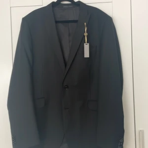 Svart kostym från Batistini - Säljer en svart kostym från Batistini, aldrig använd. Kavajen har en klassisk design med två knappar och fickor fram. Insidan av kavajen har fina detaljer med fickor och snygg sömnad. Kavajen ensam går för 250kr men lägger du 200kr extra får du ett par matchande byxor (se bild 4) och ett par snarlika byxor (se bild 5) på köpet! Även de aldrig använda.