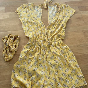 Gul blommig byxdress från American Eagle - Säljer en superfin gul blommig byxdress från American Eagle. Den har en söt öppen rygg med knytning i nacken och elastisk midja för en bekväm passform. Den är kortärmad och perfekt för sommaren. Den är i nyskick och kommer med ett matchande mid