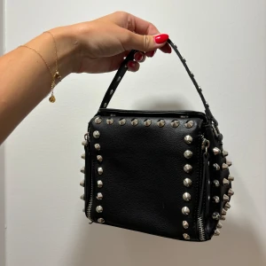 Nitväska - Nitväska. Man ser tecken på slitage men inget som stör. På baksidan är en liten bit läder avskavt se bild, även knapparna invändigt är lite röda i förgen. Kan skicka mer bilder. Axelband skickad med men notera att den är lite rostig men man kan byta 