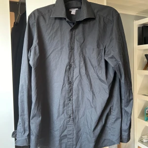 Svart långärmad skjorta - Säljer en stilren svart långärmad skjorta. Skjortan har en klassisk krage och knappar längs framsidan. Den är i bra skick. Pris går att diskuteras.
