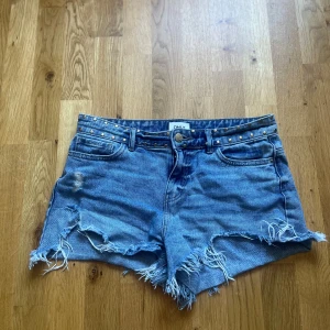 Blå jeansshorts från ONLY - Säljer ett par snygga blå jeansshorts från ONLY. De har en medelhög midja och är dekorerade med nitar både fram och bak. Shortsen har en sliten look med fransiga kanter och en liten reva på ena bakfickan. Nypris ca 400!💓