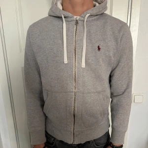 Grå Polo RalphLauren ZipHoodie - En Ljusgrå Polo Ralph Lauren Fullzip Hoodie i Välomhändetaget skick! Lite slitna ärmar. Storlek M men passar bra som S. Modellen är 182 cm och väger 75 kg. Pris öppet till förhandling!