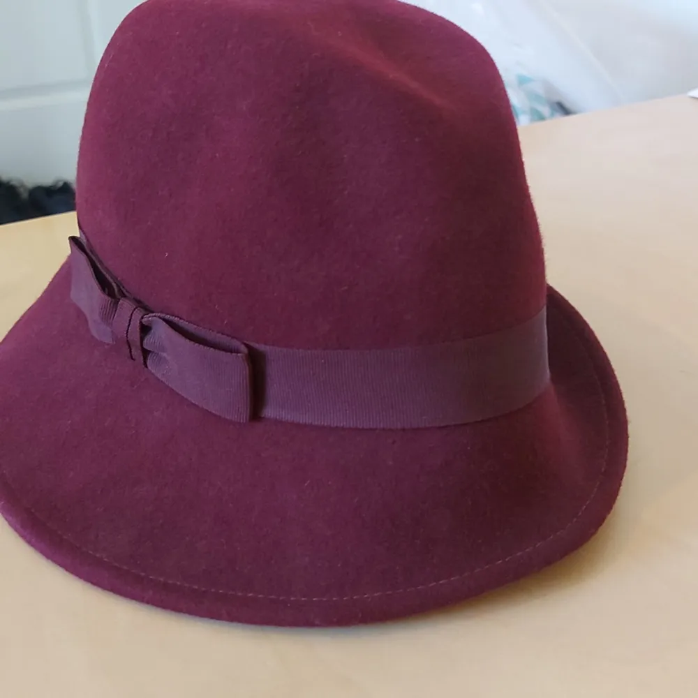 Säljer en snygg vinröd hatt med en matchande rosett på sidan. Hatten är gjord av ett mjukt material och har en klassisk form som passar perfekt för höst och vinter. Den är i dam one size från Åhléns och i nyskick. Perfekt för att ge din outfit en elegant touch!. Accessoarer.