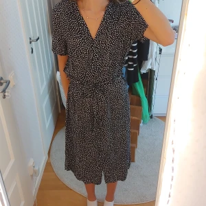 Svart prickig klänning från Vero Moda - Säljer en superfin svart klänning med vita prickar från Vero Moda. Klänningen är i storlek L och har en knytning i midjan som ger en snygg passform. Den har korta ärmar och en v-ringad hals. Perfekt för sommarens alla fester eller en dag på stan. Klänningen är i nyskick och väldigt bekväm att ha på sig. Köp den nu och var redo för sommaren! 🌸🖤🤍
