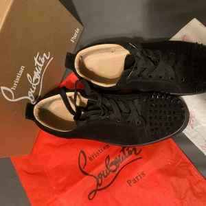 Svarta skor från Christian Louboutin - Snygga svarta sneakers från Christian Louboutin i mocka med snörning och dekorativa nitar på tån. Perfekta för att ge en edgy touch till din stil. Levereras med originalförpackning och dustbag. DM vid intresse