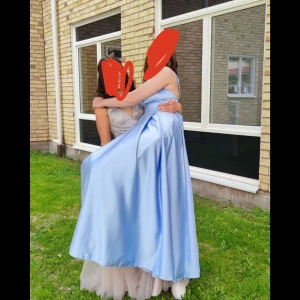 Ljusblå balklänning  - Elegant ljusblå långklänning i satin med v-ringad urringning och smala axelband. Perfekt för en bal eller festlig tillställning. Klänningen har en vacker fall och ger en lyxig känsla. Klänningen har fickor på sidan som inte syns av fallet på klänningen vilket är bra, dragkedja i ryggen så den sitter perfekt på