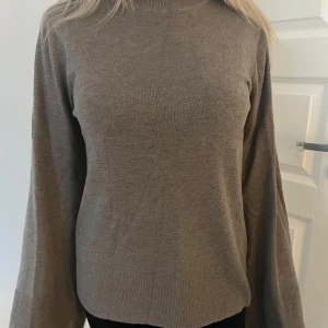 Brun/beige stickad tröja - Säljer en stilren beige/brun stickad tröja med långa ärmar. Tröjan har en lös passform och vida ärmslut som ger en trendig look. Perfekt för kyligare dagar.