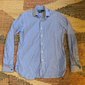 Ralph Lauren skjorta - En snygg och stilren Ralph Lauren skjorta med ett blå vit randigt mönster, storleken är L men är rätt så stor och sitter lite större en L inte som en XL dock, skjortan är i ett väldigt fint och bra skick! Hör av dig vid eventuella frågor eller funderingar!