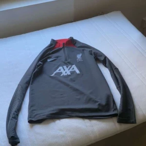 Grå Nike Liverpool tracksuit  - Säljer en grå långärmad Liverpool tracksuit. Tröjan har en halv dragkedja. Perfekt för fotbollsträning eller som en sportig vardagströja.