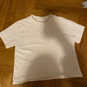 Vit t-shirt från Gina Tricot - Säljer en klassisk vit t-shirt från Gina Tricot i storlek S. Lite tajt när man tar på den över halsen, men känns inte när den väl är på. T-shirten är kortärmad och tillverkad i ett mjukt material som ger en skön känsla. Perfekt basplagg för alla tillfällen.