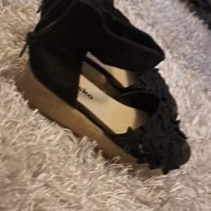 Svarta sandaler med blommig detalj - Snygga svarta sandaler med blommig detalj och dragkedja bak. Perfekta för sommarens alla tillfällen. Bekväm sula och stilren design.