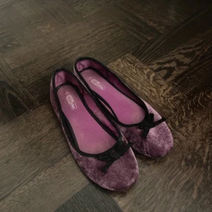  ballerinaskor  - Säljer ett par lila ballerinaskor  i sammet med en söt rosett på ovansidan. Skorna har en mjuk och bekväm passform, perfekt för en stilren look. Från din sko